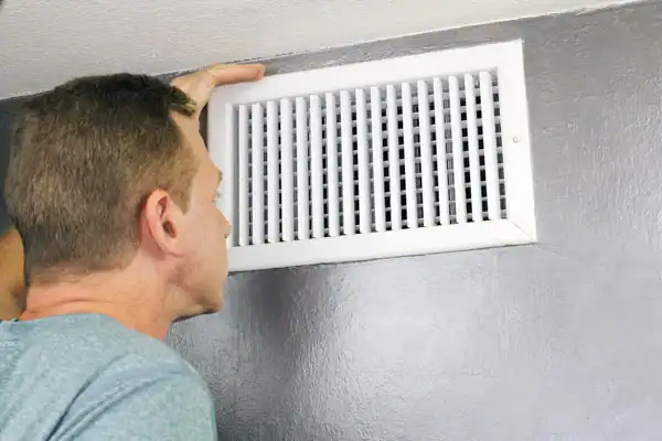 Person inspecting a white wall air vent.