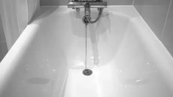 A white bathtub with a showerhead and faucet. A plug chain is draped into the tub.