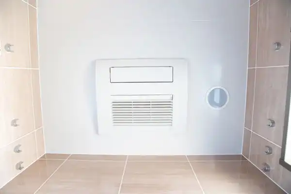 A bathroom ceiling with a white exhaust vent and beige tiles.