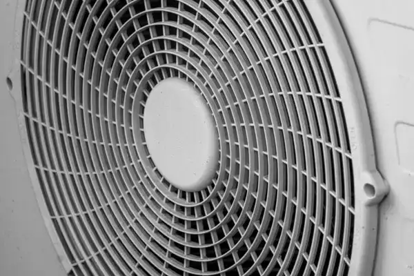 Close-up of a circular fan grille with a grid pattern, mounted on a white surface.