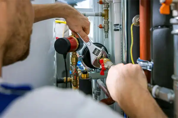 A person uses a wrench to adjust valves on metal pipes in a mechanical or boiler room.