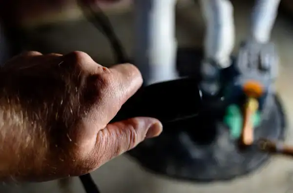 A person holding a black TV remote, pointing towards a figurine or object in the distance.