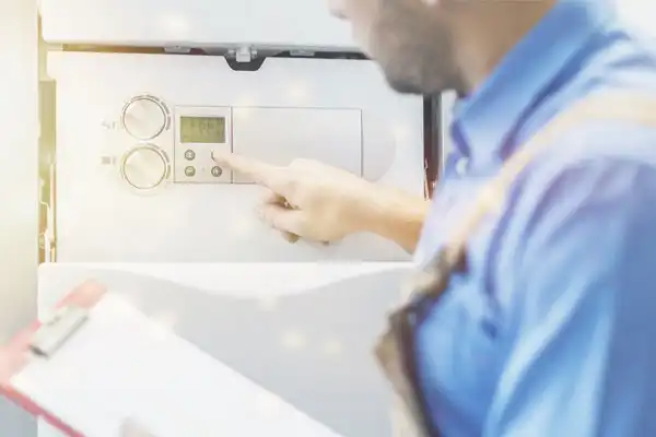 A person in a blue shirt adjusts the settings on a wall-mounted control panel while holding a clipboard.