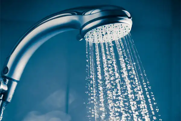Close-up of a showerhead with water spraying out against a blue background.