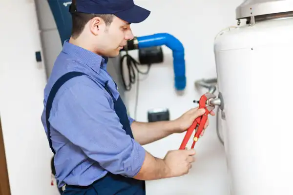 A person in a blue uniform uses pliers to adjust a fitting on a white tank.