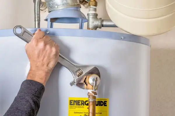 A person skillfully using a wrench to tighten a nut on a water heater, with an energy guide label prominently displayed, showcases the meticulous process of water heater repair.