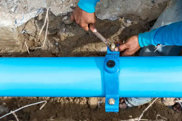 Person tightening a bolt on a blue underground pipe using a wrench.