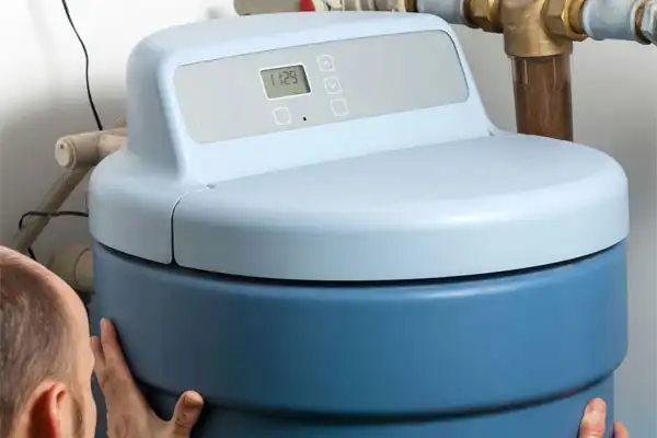 Person adjusting a blue water softener unit with digital controls on top.