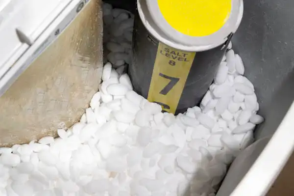 Salt pellets surround a cylindrical container with a yellow lid inside a salt storage tank.