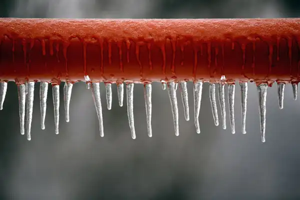 Icicles hanging from a red pipe, with a blurred gray background.